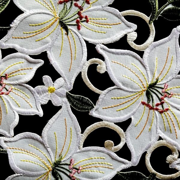 Close-up of ornate white floral embroidery on black fabric with intricate patterns.
