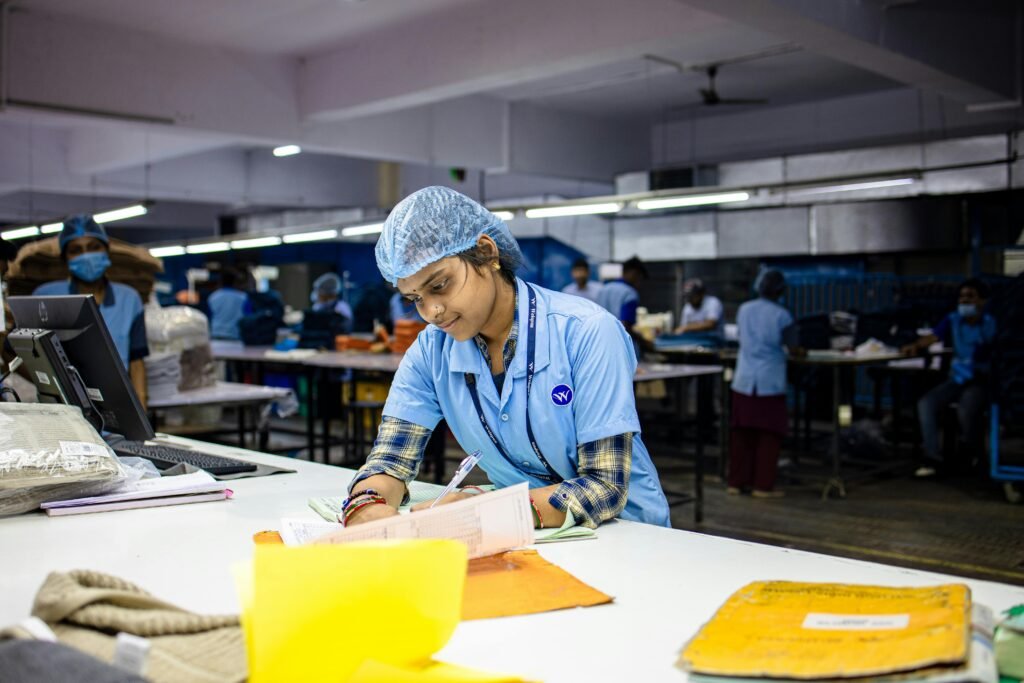 Female factory worker wearing uniform and hairnet, focused on writing tasks in textile environment.