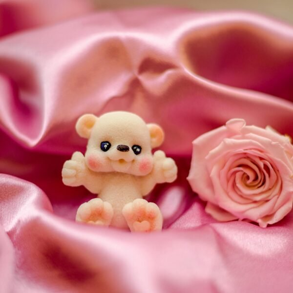 Adorable plush bear toy with a pink rose resting on luxurious pink satin fabric. Ideal for themes of love and romance.