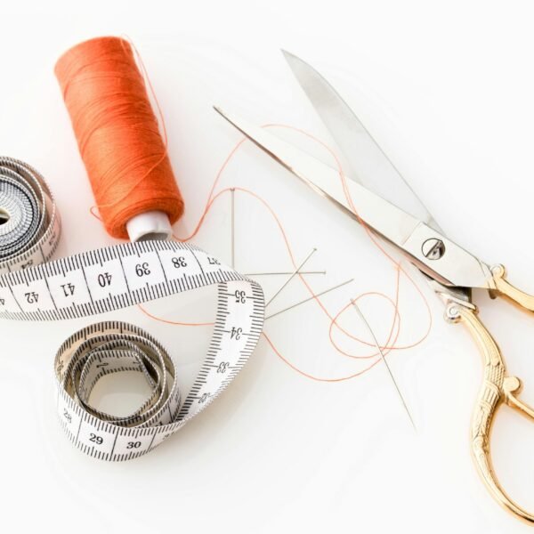 Photo of sewing essentials: scissors, thread, needles, and tape measure on a white background.