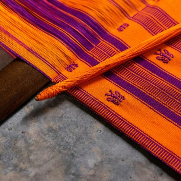 Close-up of a colorful handwoven Mexican textile in orange and purple hues.