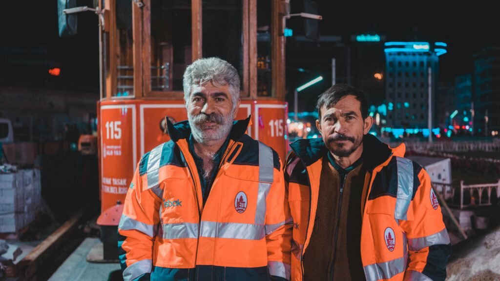 Two tram workers in reflective uniforms pose at night in Istanbul, Turkey.